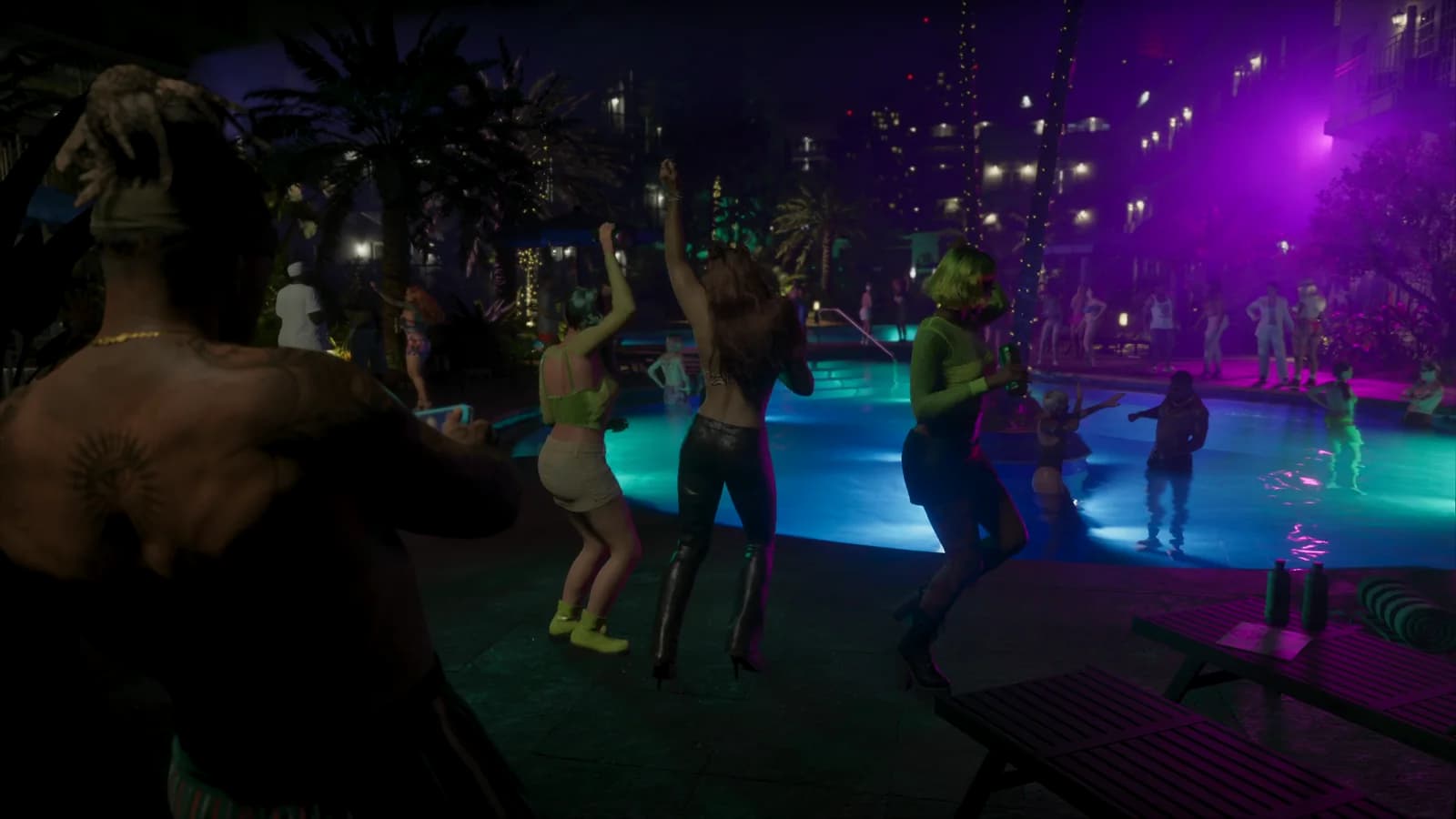 Un uomo a torso nudo con un tatuaggio sulla schiena filma con il telefono una festa in piscina illuminata di turchese e viola, con persone che ballano in acqua.