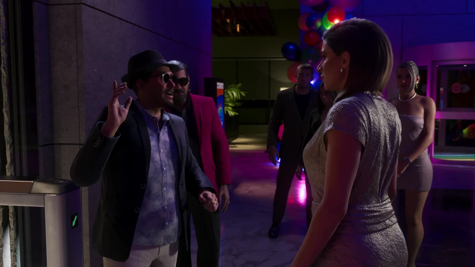 Nell'atrio di un edificio, l'uomo con il fedora fa un gesto con le dita mentre una donna in abito metallizzato passa davanti a lui tra altri ospiti eleganti.