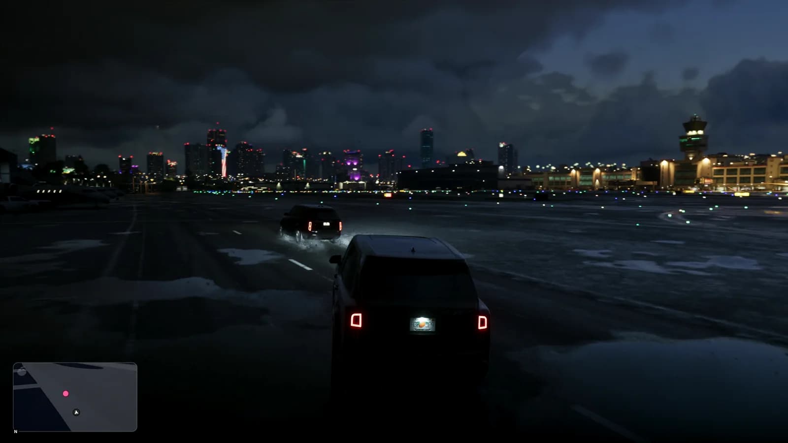 Due suv neri attraversano di notte l'area dell'aeroporto in direzione della città, con lo skyline illuminato sullo sfondo e la minimappa di gioco visibile in basso a sinistra.
